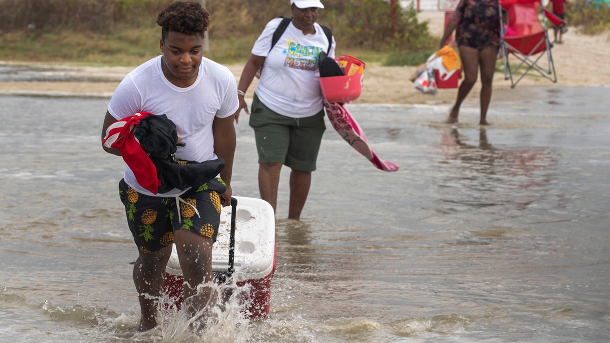 Tyler Heads totes his belongings through tidewaters as he and other beachgoers cross the flooding Stewart Beach parking lot in Galveston, Texas on Saturday, Sept. 19, 2020.