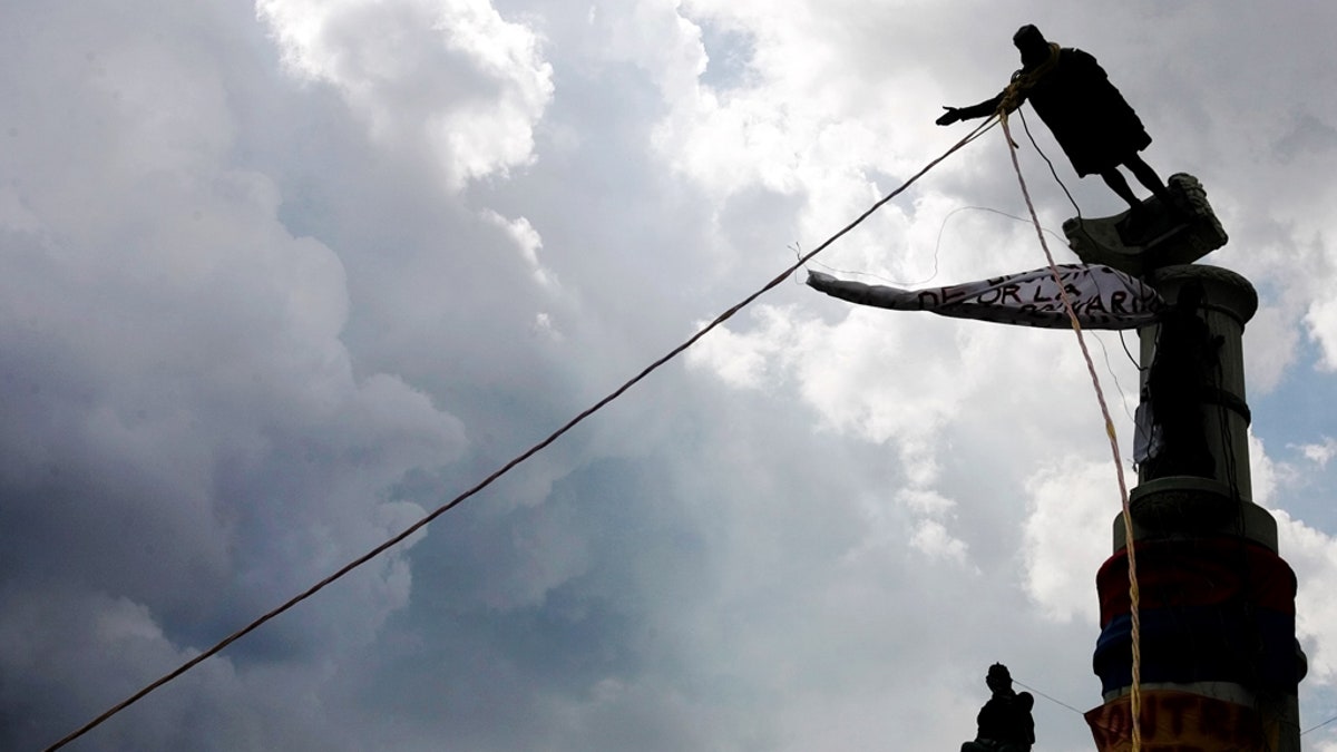 Venezuelan demonstrators use ropes to topple a Christopher Columbus statue in Caracas, October 12, 2004. REUTERS/Jorge Silva
