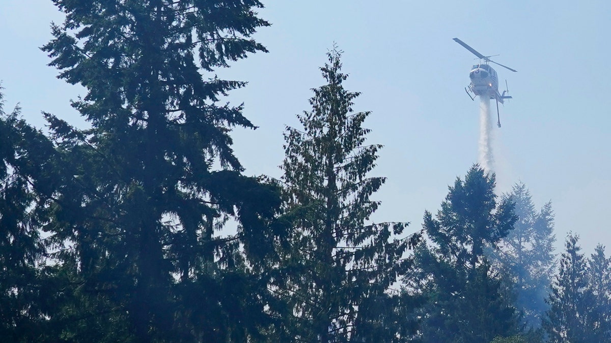A helicopter makes a water drop, Wednesday, Sept. 9, 2020, on a hotspot of a wildfire burning in Bonney Lake, Wash., south of Seattle.