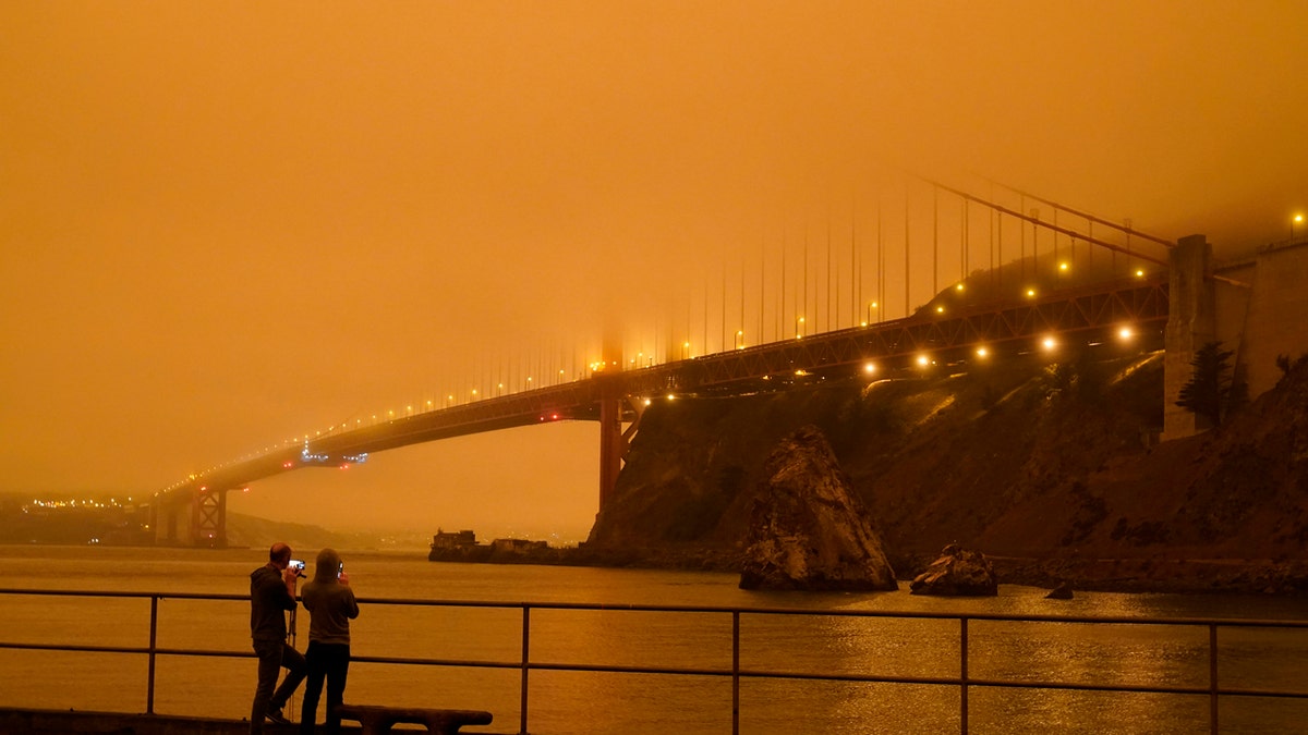 Patrick Kenefick, left, and Dana Williams, both of Mill Valley, Calif., record the darkened Golden Gate Bridge covered with smoke from wildfires Wednesday, Sept. 9, 2020, from a pier at Fort Baker near Sausalito, Calif. The photo was taken at 9:47 a.m. in the morning.