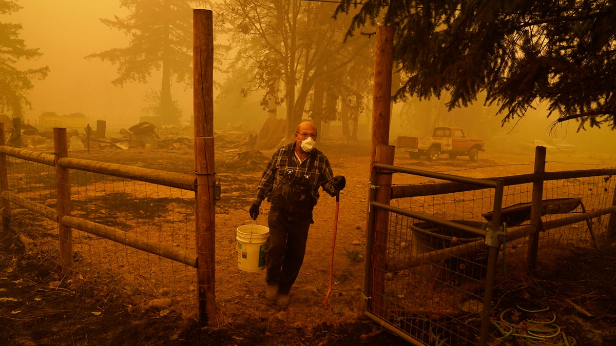 George Coble carries a bucket of water to put out a tree still smoldering on his property destroyed by a wildfire Saturday, Sept. 12, 2020, in Mill City, Ore.