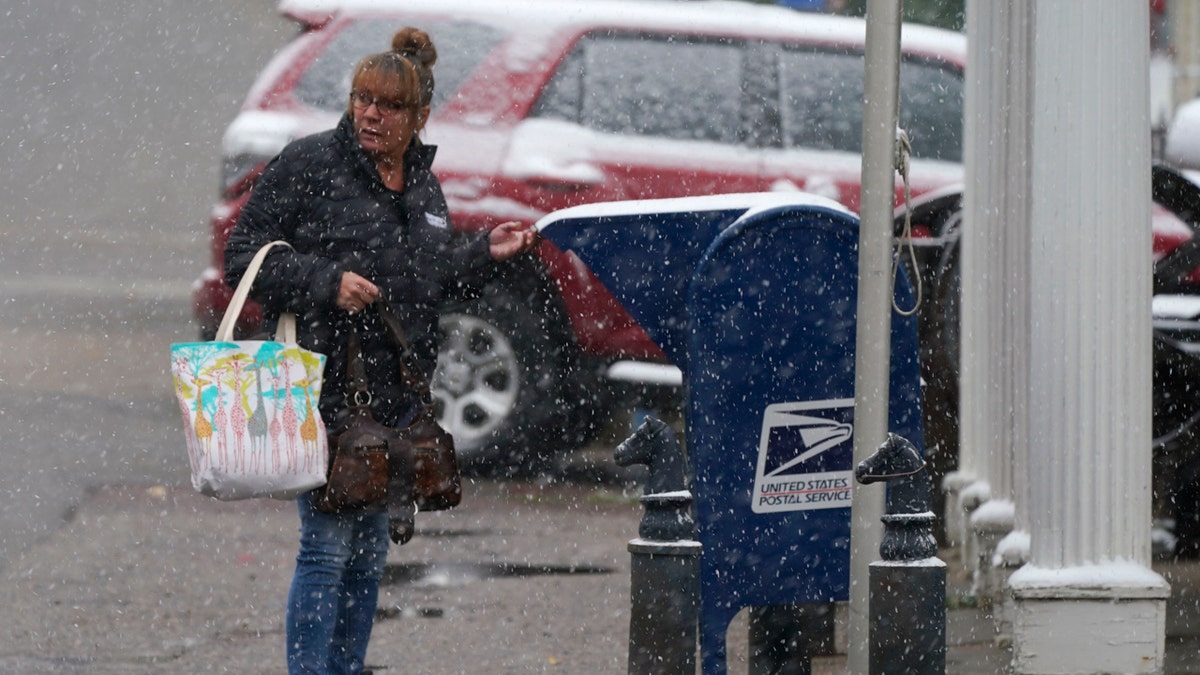 A woman drops off a letter in a mailbox in front of the post office as a storm packing high winds and snow sweeps through the intermountain West Tuesday, Sept. 8, 2020, in Georgetown, Colo.