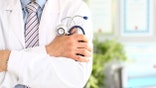Close up of crossed male hands with medical instrument for listening to action of heart or breathing. Medicine and health care concept.Blurred background