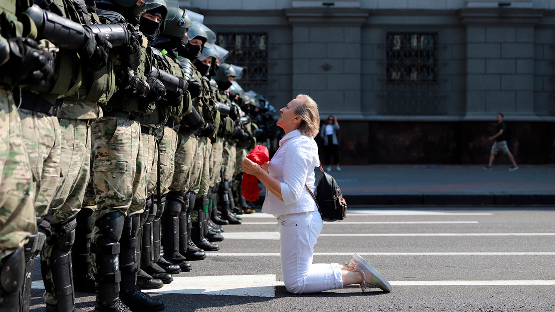 A woman kneels in front of a riot police line as they block Belarusian opposition supporters in Minsk, Belarus, Aug. 30, 2020. 