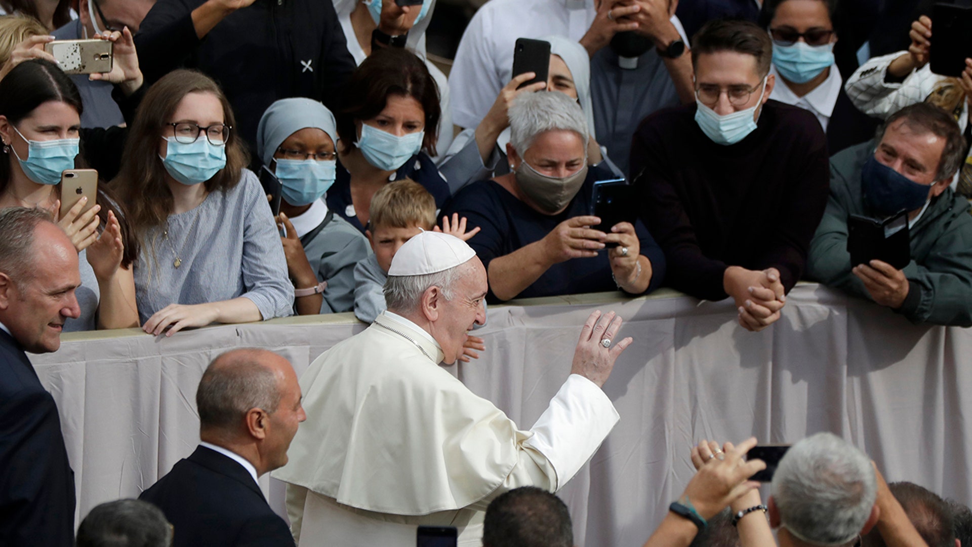 People wear face masks to prevent the spread of COVID-19 while Pope Francis waves as he arrives for his first general audience with the faithful since February at the Vatican, Sept. 2, 2020. 