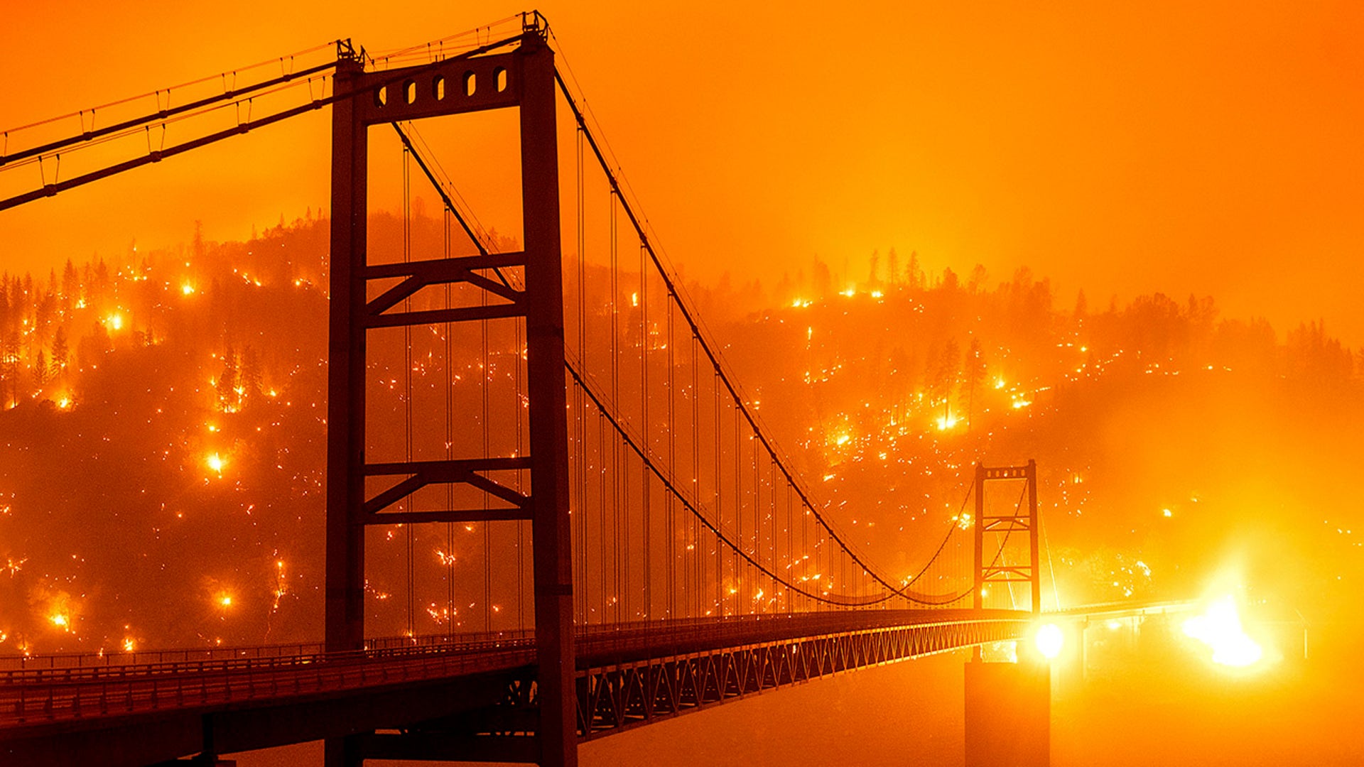 In this image taken with a slow shutter speed, embers light up a hillside behind the Bidwell Bar Bridge as the Bear Fire burns in Oroville, Calif., on Wednesday, Sept. 9, 2020. The blaze, part of the lightning-sparked North Complex, expanded at a critical rate of spread as winds buffeted the region.
