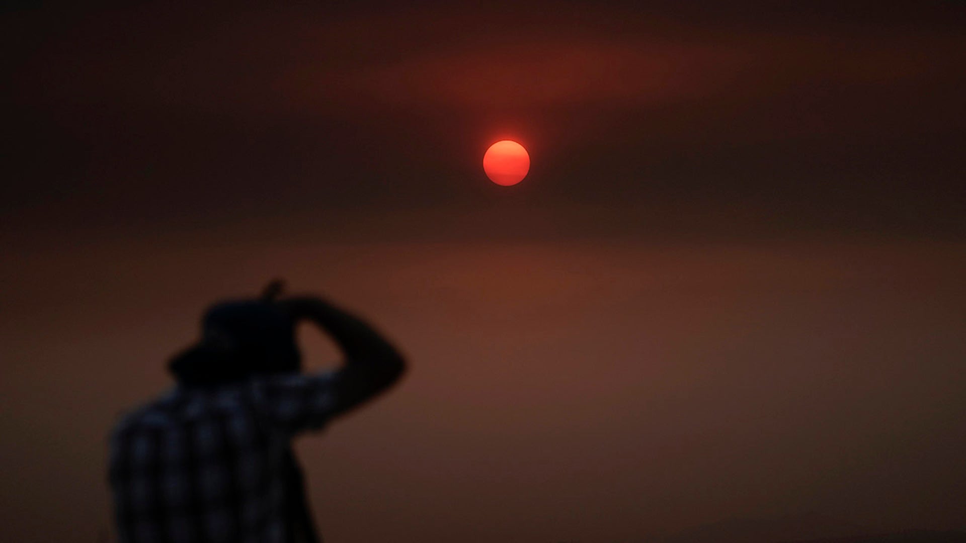 Jason Anderson, 42, takes pictures as the sun is visible through thick smoke generated by the Bobcat Fire in San Dimas, Calif., Wednesday, Sept. 9, 2020. Hazy clouds of smoke from dozens of wildfires darkened the sky to an eerie orange glow over much of the West Coast on Wednesday, keeping street lights illuminated during the day and putting residents on edge.