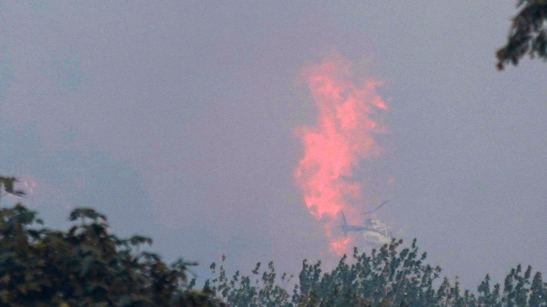 A helicopter with a water bucket flies near a burning hillside, Tuesday, Sept. 8, 2020, near Sumner, Wash., south of Seattle.