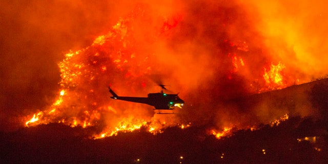 FILE - In this Saturday, Sept. 5, 2020, file photo, a helicopter prepares to drop water at a wildfire in Yucaipa, Calif. A couple’s plan to reveal their baby’s gender at a party went up in smoke Saturday at El Rancho Dorado Park in Yucaipa, when a pyrotechnical device they used sparked a wildfire that has burned thousands of acres. (AP Photo/Ringo H.W. Chiu, File)