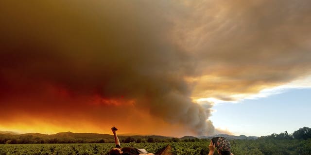 FILE - In this Aug. 20, 2020, file photo, Thomas Henney, left, and Charles Chavira watch a plume spread over Healdsburg, Calif., as the LNU Lightning Complex fires burn. Two unusual weather phenomena combined to create some of the most destructive wildfires the West Coast states have seen in modern times. (AP Photo/Noah Berger, File)