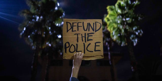 A protester holds up a sign as a police helicopter flies by in front of the South Los Angeles Sheriff's Department during protests following the death of Dijon Kizzee.