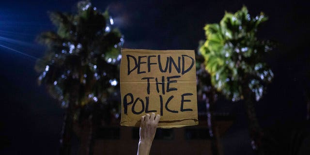 A protester holds up a sign as a police helicopter flies by in front of the South Los Angeles Sheriff's Department during protests following the death of Dijon Kizzee.