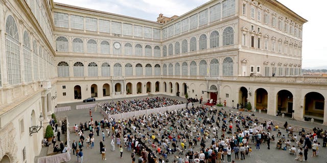 Faithful listen to Pope Francis, the white figure sitting at center right, during his general audience Wednesday at the San Damaso courtyard, at the Vatican, the first since February when the coronavirus pandemic began. (AP Photo/Andrew Medichini)