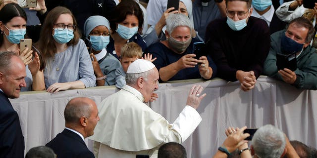 People wear face masks to prevent the spread of COVID-19 while Pope Francis waves as he arrives for his first general audience. (AP Photo/Andrew Medichini)