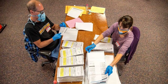FILE: In this photo provided by Wisconsin Watch, election workers Jeff and Lori Lutzka, right, process absentee ballots at Milwaukee's central count facility on Aug. 11, 2020. Wisconsin elections officials are taking multiple steps to make mail-in voting smoother in November, when most people are expected to vote absentee. (Will Cioci/Wisconsin Watch via AP)