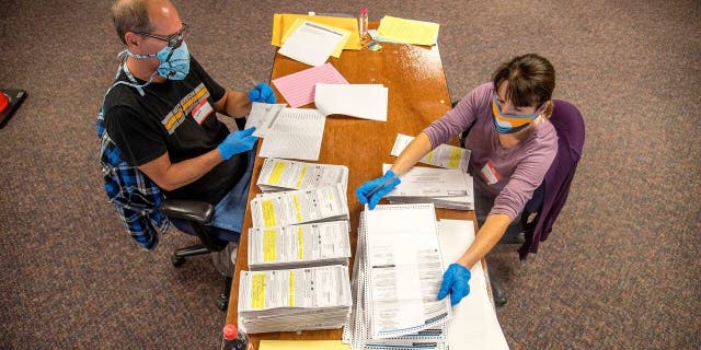 In this photo provided by Wisconsin Watch, election workers Jeff and Lori Lutzka, right, process absentee ballots at Milwaukee's central count facility on Aug. 11, 2020. (Will Cioci/Wisconsin Watch via AP)
