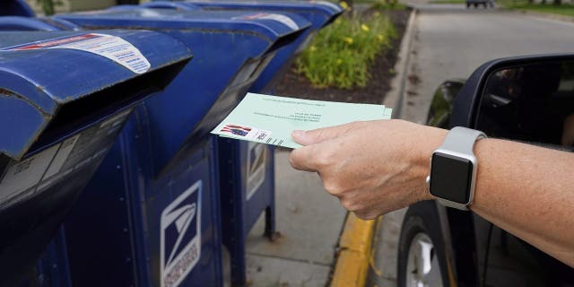 FILE - In this Tuesday, Aug. 18, 2020, file photo, a person drops applications for mail-in-ballots into a mail box in Omaha, Neb.