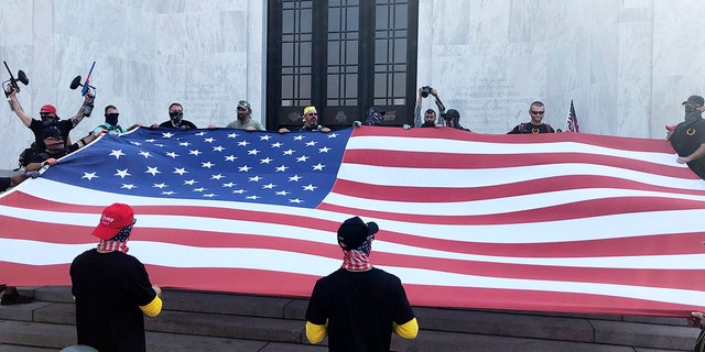 Right-wing protesters unfurl a flag on the steps of Oregon State Capitol for a pro-Donald Trump rally at the Capitol in Salem, Ore. on Monday, Sept. 7, 2020. (AP Photo/Andrew Selsky)