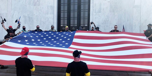 Right-wing protesters unfurl a flag on the steps of Oregon State Capitol for a pro-Donald Trump rally at the Capitol in Salem, Ore. on Monday, Sept. 7, 2020. (AP Photo/Andrew Selsky)