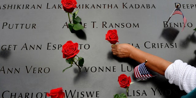 In this Sept. 11, 2014, file photo, a woman places flowers in the inscribed names along the edge of the North Pool during memorial observances on the 13th anniversary of the Sept. 11, 2001 terror attacks on the World Trade Center in New York. The coronavirus pandemic has reshaped how the U.S. is observing the anniversary of 9/11. (AP Photo/Justin Lane, Pool, File)