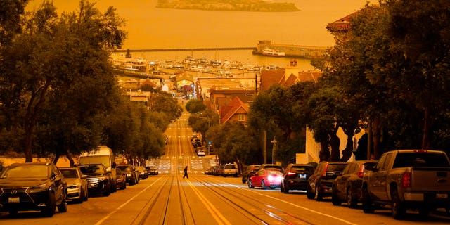 Under darkened skies from wildfire smoke, a man crosses Hyde Street with Alcatraz Island and Fisherman's Wharf in the background Sept. 9, in San Francisco. (AP Photo/Eric Risberg)