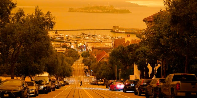 Under darkened skies from wildfire smoke, a man crosses Hyde Street with Alcatraz Island and Fisherman's Wharf in the background Wednesday, Sept. 9, in San Francisco. The picture was taken in the middle of the day at 12:29 p.m. (AP Photo/Eric Risberg)