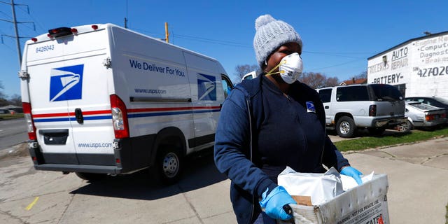 FILE: A United States Postal Service worker makes a delivery with gloves and a mask in Warren, Mich. 