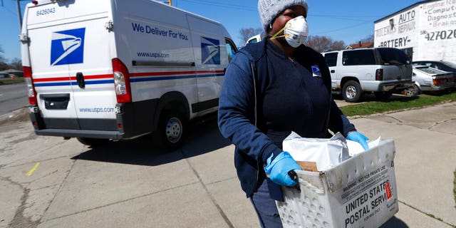 FILE: A United States Postal Service worker makes a delivery with gloves and a mask in Warren, Mich.