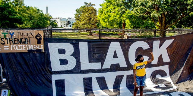 The White House is visible behind a woman who holds her fist up as she poses for a photograph with a large banner that reads Black Lives Matter hanging on a security fence in Washington, after days of protests over the death of George Floyd. 