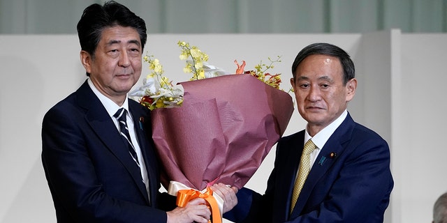 Japan's Prime Minister Shinzo Abe, left, receives flowers from Chief Cabinet Secretary Yoshihide Suga after Suga was elected as new head of Japan's ruling party at the Liberal Democratic Party's (LDP) leadership election Monday, Sept. 14, 2020, in Tokyo. The ruling LDP chooses its new leader in an internal vote to pick a successor to Prime Minister Shinzo Abe, who announced his intention to resign last month due to illness. (AP Photo/Eugene Hoshiko, Pool)