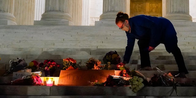 People lay flowers and light candies outside the Supreme Court Friday, Sept. 18, 2020, in Washington, after the Supreme Court announced that Supreme Court Justice Ruth Bader Ginsburg died of metastatic pancreatic cancer at age 87. (AP Photo/Alex Brandon)