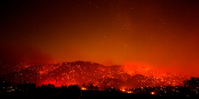 Flames dot a hill under a smoky sky from the Bobcat Fire in Juniper Hills, Calif., Friday, Sept. 18, 2020. (AP Photo/Ringo H.W. Chiu)