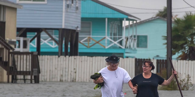Michael Koudelka and Carol Kelly walk through tidal flood waters on East Hunter Drive in the unincorporated community of Freddiesville near Bayou Vista, Texas on Monday, Sept. 21, 2020. Tidal surge as well as rain showers from the storm continued to inundate low-lying area around Galveston County, Texas. (Stuart Villanueva/The Galveston County Daily News via AP)