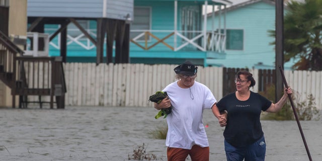 Michael Koudelka and Carol Kelly walk through tidal flood waters on East Hunter Drive in the unincorporated community of Freddiesville near Bayou Vista, Texas on Monday, Sept. 21, 2020. Tidal surge as well as rain showers from the storm continued to inundate low-lying area around Galveston County, Texas. (Stuart Villanueva/The Galveston County Daily News via AP)