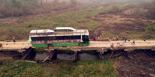 Tourists sit on a bridge railing after their sports fishing tour bus became stuck on a bridge damaged by wildfires, on the Trans-Pantanal highway in the Pantanal wetlands near Pocone, Mato Grosso state, Brazil, Friday, Sept. 11, 2020. Both sides of the highway usually feature pools of water, even in its dry season. (AP Photo/Andre Penner)