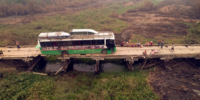 Tourists sit on a bridge railing after their sports fishing tour bus became stuck on a bridge damaged by wildfires, on the Trans-Pantanal highway in the Pantanal wetlands near Pocone, Mato Grosso state, Brazil, Friday, Sept. 11, 2020. Both sides of the highway usually feature pools of water, even in its dry season. (AP Photo/Andre Penner)