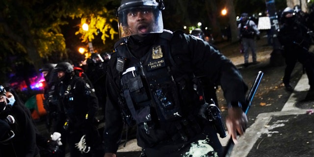 A Portland police officer pushes back protesters, Saturday, Sept. 26, 2020, in Portland. (AP Photo/John Locher)