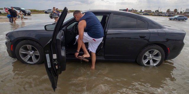 Houston resident Lupe Don removes his flip-flops while moving his car from the flooding Stewart Beach parking lot in Galveston, Texas on Saturday, Sept. 19, 2020.