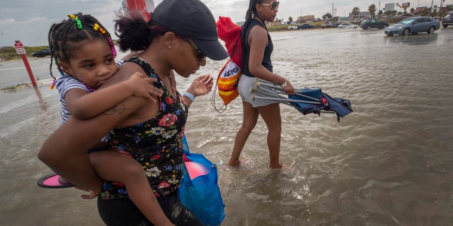 Stacey Young gives her daughter, Kylee Potts, a piggyback ride across the flooding Stewart Beach parking lot in Galveston, Texas on Saturday, Sept. 19, 2020.