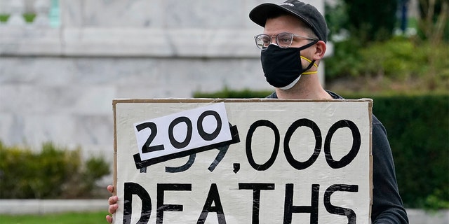 A man holds up a sign on the coronavirus deaths in America at a rally near the debate hall, Tuesday, Sept. 29, 2020, in Cleveland. The first presidential debate between Republican candidate President Donald Trump and Democratic candidate and former Vice President Joe Biden is being held in Cleveland Tuesday. (AP Photo/Tony Dejak)