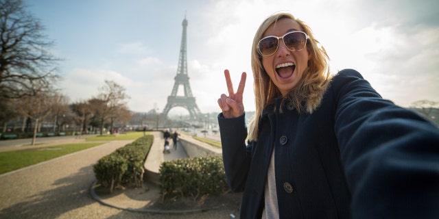 Woman takes selfie in front of the Eiffel Tower in Paris, France.