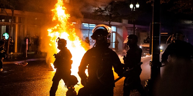 Portland police walk past a fire started by a Molotov cocktail thrown at police on September 23, 2020 in Portland, United States. (Photo by Nathan Howard/Getty Images)