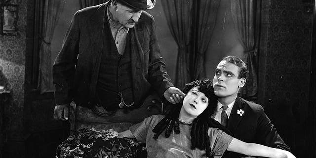 Actress Mabel Normand (1894-1930) gets her ear pulled by a possessive father in this scene from the 1923 film 'The Extra Girl'. Ralph Graves (1901-1977) sits next to her on the sofa.