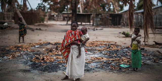 A woman holds her younger child while standing in a burned out area in the recently attacked village of Aldeia da Paz outside Macomia, on August 24, 2019. - On August 1, the inhabitants of Aldeia da Paz joined the long list of victims of a faceless Islamist group that has been sowing death and terror for nearly two years in the north of the country, which welcomes from September 4 the Pope. (Photo by MARCO LONGARI / AFP) (Photo by MARCO LONGARI/AFP via Getty Images)