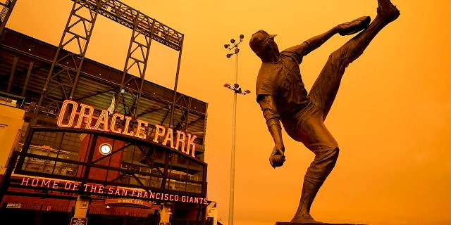 Wildfire smoke darkens the sky over a statue of former San Francisco Giants pitcher Juan Marichal outside Oracle Park before a baseball game between the Giants and the Seattle Mariners on Wednesday, Sept. 9, 2020, in San Francisco. People from San Francisco to Seattle woke Wednesday to hazy clouds of smoke lingering in the air, darkening the sky to an eerie orange glow that kept street lights illuminated into midday, all thanks to dozens of wildfires throughout the West. (AP Photo/Tony Avelar)
