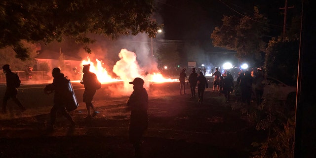 Flames rise from a street after a liquid had been spread and lit, Saturday, Sept. 5, 2020, during protests in Portland, Ore. Some protesters, at, left, move back as police, at background right, advance. (Associated Press)