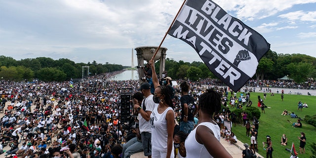 FILE - In this Aug. 28, 2020, file photo, a woman holds a "Black Lives Matter," flag during the March on Washington at the Lincoln Memorial in Washington, on the 57th anniversary of the Rev. Martin Luther King Jr.'s "I Have A Dream" speech. Ahead of Labor Day, major U.S. labor unions say they are considering work stoppages in support of the Black Lives Matter movement. (AP Photo/Alex Brandon, File)