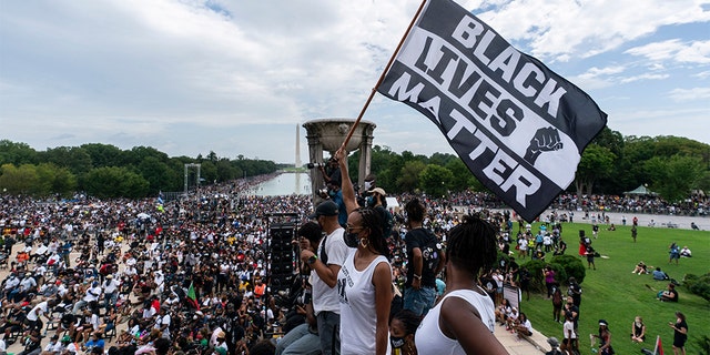 FILE - In this Aug. 28, 2020, file photo, a woman holds a "Black Lives Matter," flag during the March on Washington at the Lincoln Memorial in Washington, on the 57th anniversary of the Rev. Martin Luther King Jr.'s "I Have A Dream" speech. Ahead of Labor Day, major U.S. labor unions say they are considering work stoppages in support of the Black Lives Matter movement. (AP Photo/Alex Brandon, File)