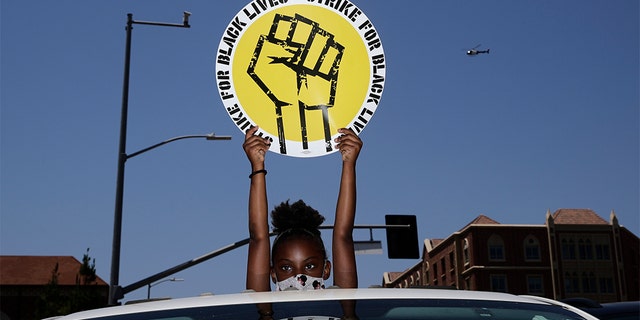 FILE - In this July 20, 2020, file photo, Audrey Reed, 8, holds up a sing through the sunroof of a car during a rally in Los Angeles. Ahead of Labor Day, major U.S. labor unions say they are considering work stoppages in support of the Black Lives Matter movement. (AP Photo/Jae C. Hong, File)
