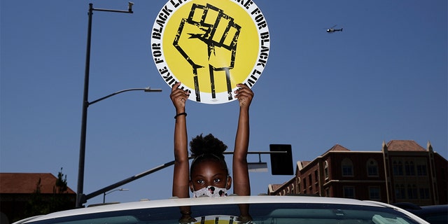 FILE - In this July 20, 2020, file photo, Audrey Reed, 8, holds up a sing through the sunroof of a car during a rally in Los Angeles. Ahead of Labor Day, major U.S. labor unions say they are considering work stoppages in support of the Black Lives Matter movement. (AP Photo/Jae C. Hong, File)